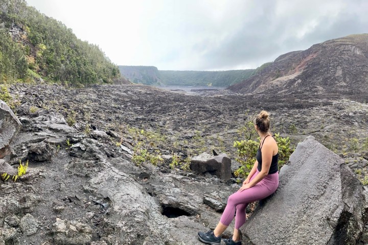 Person sitting on rock overlooking rocky landscape with cloudy sky.
