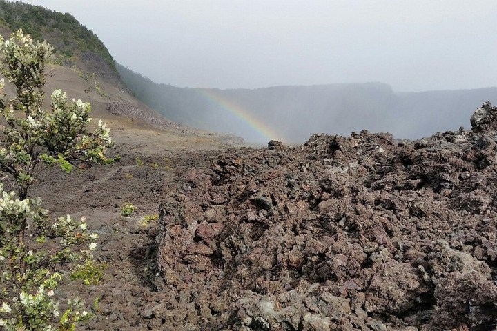 Lava rock landscape with sparse plants and a faint rainbow in the sky.