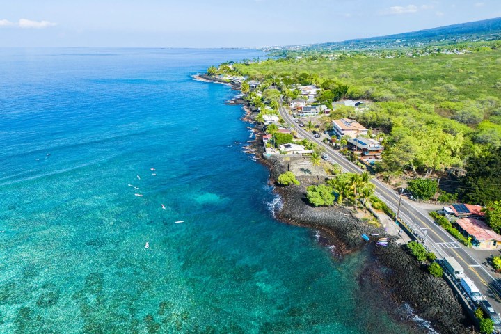 Aerial view of a coastal road beside turquoise ocean and lush green landscape.
